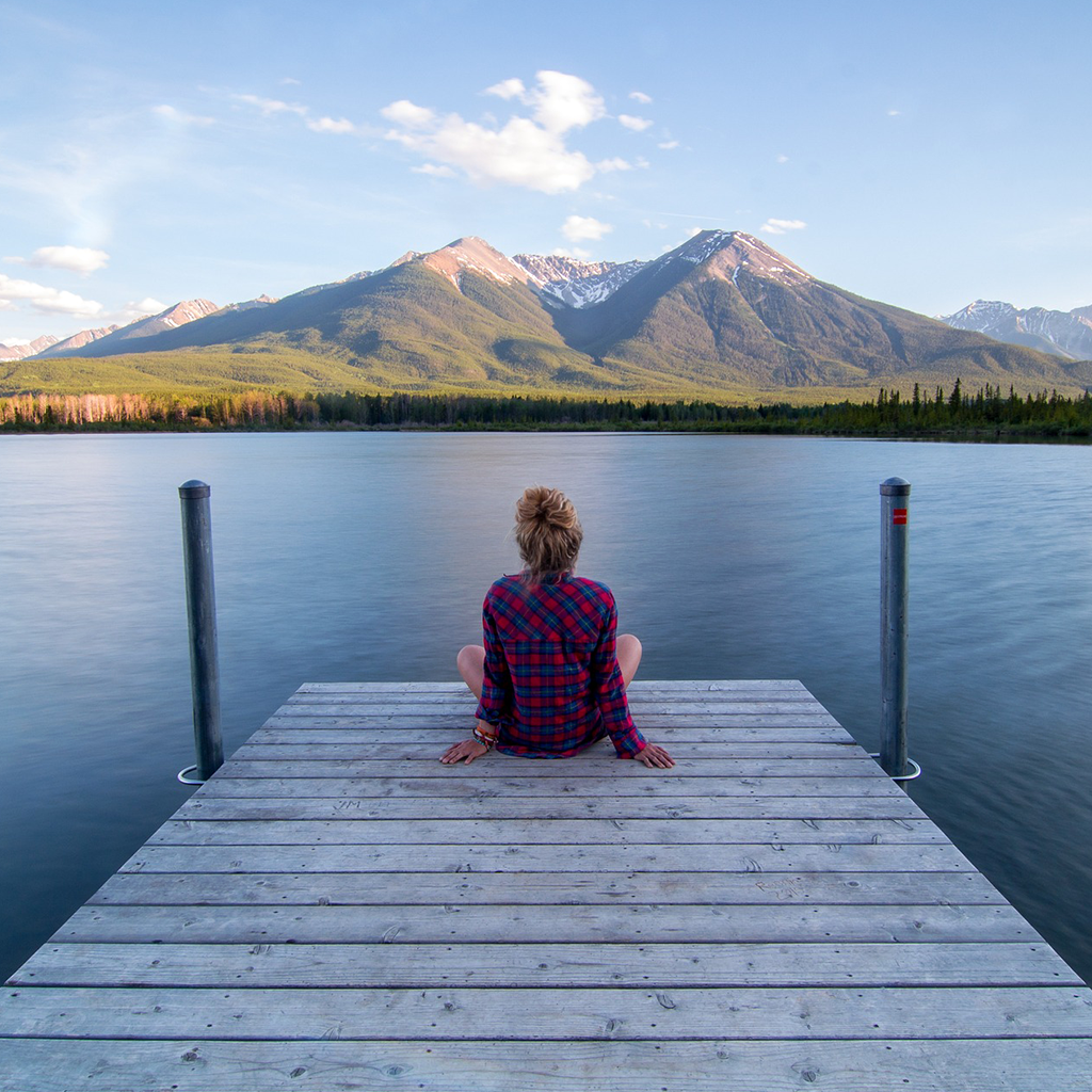 donna seduta su una passerella in legno davanti un lago e montagne